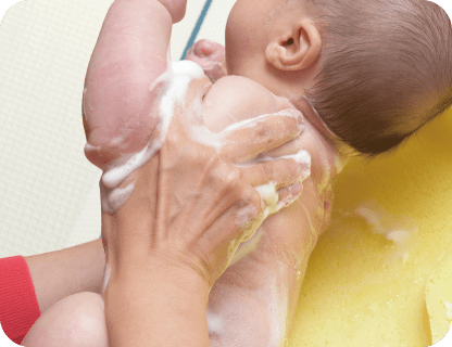 Вымойте ребенка сзади, пока он лежит на боку.